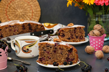 Walnut pie with black currant is located on a plate on a dark background. In the foreground is a piece of cake and a cup of coffee