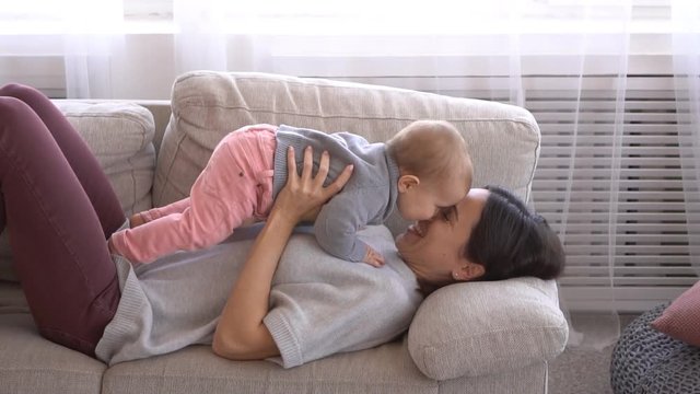 Mother playing with her infant baby girl on sofa