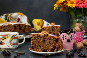 Homemade pie with black currant and walnuts is located on a plate on a dark background