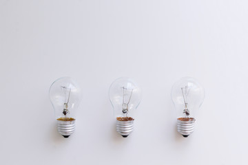 Three light bulbs on the white table. Electricity consumption, intellectual property concept. Top view, flat lay, copy space