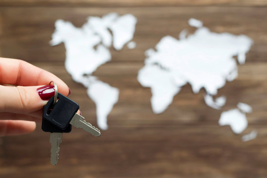 Hand holding keys and world map cutted from white paper on the wooden background. Management, security, discovery concept. Close-up, soft focus, copy space, mock up