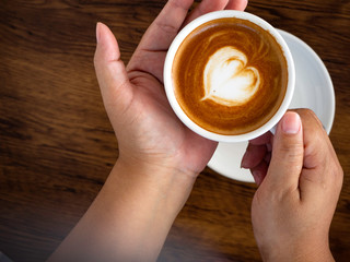 Girl holding cup of cafe latte on wooden table