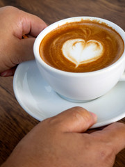 Girl holding cup of cafe latte on wooden table