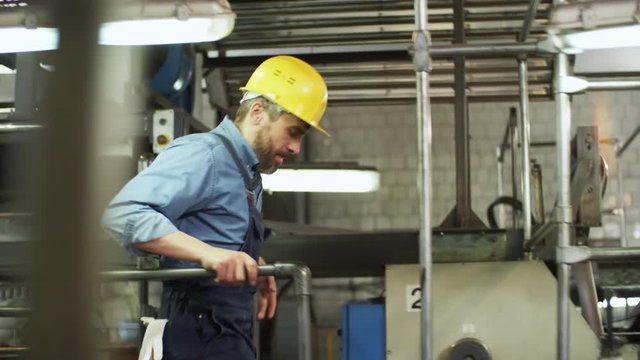 Tracking shot of factory worker in hardhat and uniform walking through industrial plant