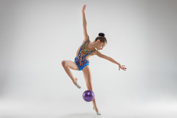 The teen female little girl doing gymnastics exercises with ball on a gray studio background. The...