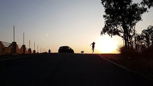 A silhouetted boy running and jumping up during sunset in slow motion