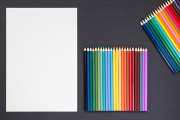 blank paper sheet and colored pencils on black background. Copy space, white surface, mockup. concept of creativity