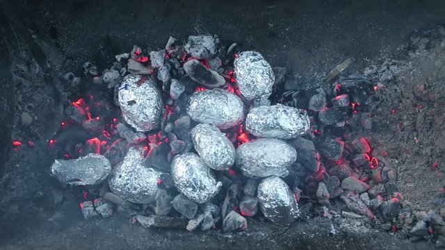 Close up of bonfire with orange and yellow flames and firewood and Baked potatoes covered with aluminum foil, Lag Baomer Jewish holiday bonfire celebration tradition of roasting Potatoes in fire