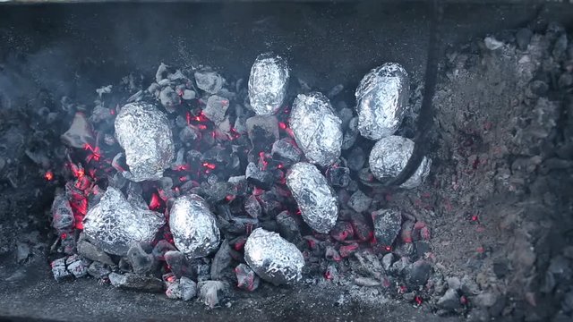 Close up of bonfire with orange and yellow flames and firewood and Baked potatoes covered with aluminum foil, Lag Baomer Jewish holiday bonfire celebration tradition of roasting Potatoes in fire