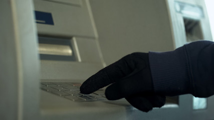 Mans hand in gloves inserting pin code, stealing money from bank account, atm