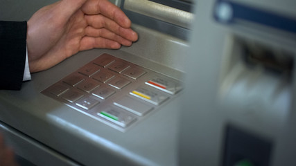 Man hiding keyboard of automated teller machine while inserting his pin code