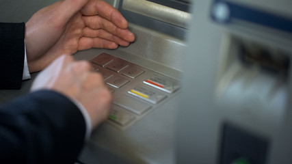 Fototapeta premium Male hiding keyboard of ATM while inserting his pin code for security, password