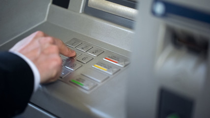 Businessman entering his pin code on keyboard of ATM, banking services, finance