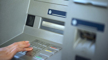 Female bank client checking account balance on ATM, entering password, finance
