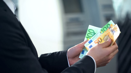 Male counting euros withdrawn from ATM, good service, business trip to Europe