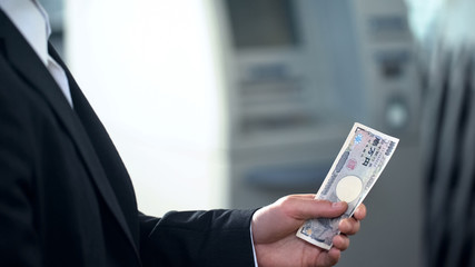 Man holding Japanese Yen banknotes withdrawn from ATM, good service, travelling