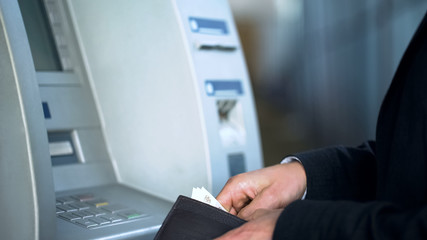 Male hands putting banknotes in purse, withdrawing money from bank account, ATM