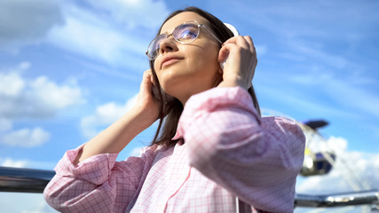 Young woman listening to music via headphones on the street, audio application