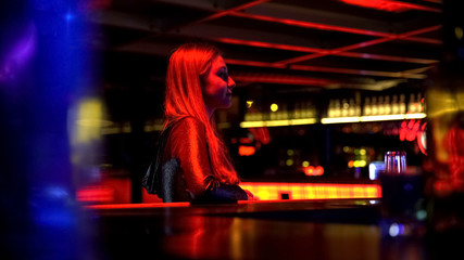 Confident beautiful young girl sitting in night club near bar, evening party