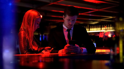 Gadget addicted couple using their smart phone in bar, lack of communication