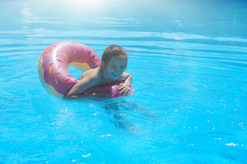 Girl teenager in a swimsuit swims with an inflatable ring in the pool with blue water.