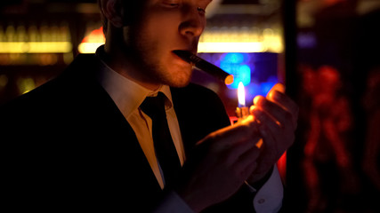 Young confident businessman setting fire to cigar, elite bar, nightlife for rich