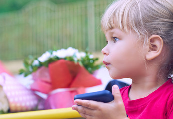 Baby girl holding a mobile phone. Little Caucasian girl playing with smartphone in summer park. Child learning how to use modern electronic devices