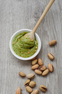 The concept of healthy food, pistachio paste and unpeeled salted pistachios, wooden spoon on a wooden background. Components for cooking.
