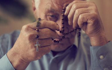 Praying hands of an old man holding rosary beads. - 235910623
