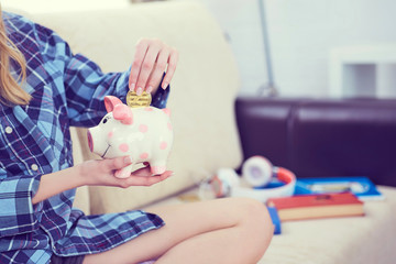 Young girl sitting on couch and putting litecoin in piggybank.
