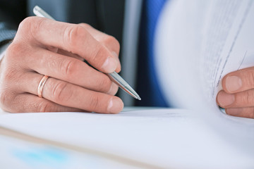 Businessman in dark suit sitting at office desk signing a contract with shallow focus on signature.