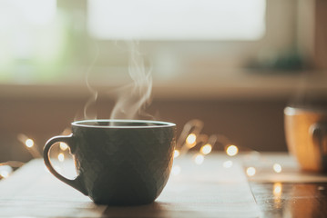 Hot cup of tea or coffee. cup with steam on the table, against the background of the lights