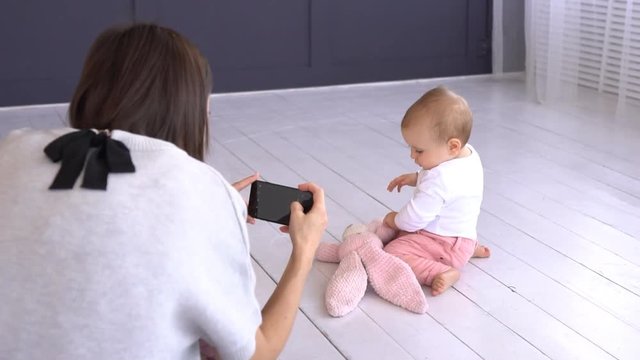 Mother photographing playful baby girl using mobile phone camera