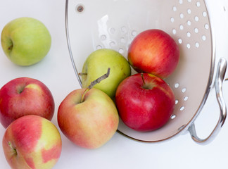 Fresh red apples in a collander / bowl scattered on white surface