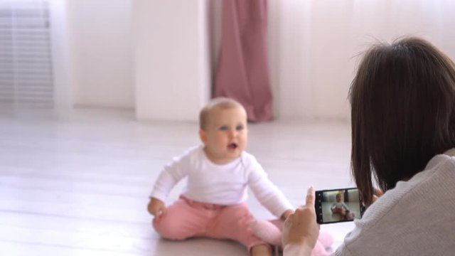 Mother photographing playful baby girl using mobile phone camera