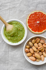 The concept of healthy food, pistachio paste, peeled and unpeeled salted pistachios, grapefruit, wooden spoon on a light background. Components for cooking.