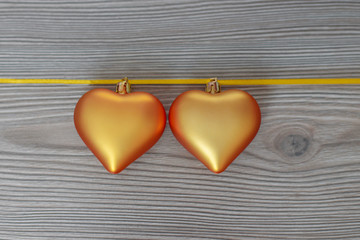 Christmas still life with love for loved ones, two golden hearts on one gold ribbon on a wooden background. Valentine's Day Gift