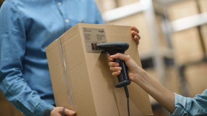 Female Inventory Manager Scans Cardboard Box and with Barcode Scanner, Male Worker Holds Package....