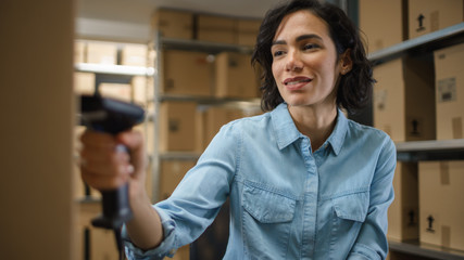 Female Inventory Manager Scans Cardboard Box and with Barcode Scanner. In the Background Rows of...