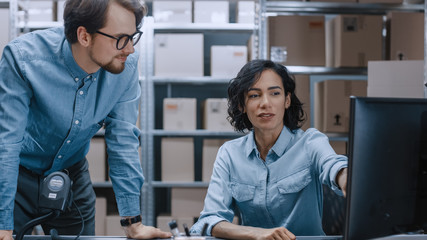 Male and Female Warehouse Inventory Managers Talking, Using Personal Computer and Checking Stock....