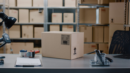 Cardboard Box Package Standing on the Table of the Warehouse where Rows of Shelves with Parcels Waiting to be Shipped and Delivered.