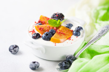 Healthy food, snacks or breakfast. Homemade Greek yogurt with blueberries, blackberries, persimmons and mint. On a concrete stone table.