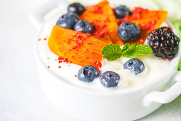 Healthy food, snacks or breakfast. Homemade Greek yogurt with blueberries, blackberries, persimmons and mint. On a concrete stone table.