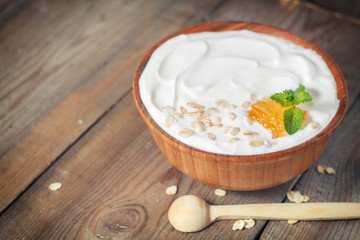 Greek yogurt with oat flakes and orange jam in a wooden bowl on a rustic wooden table.