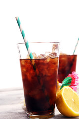 Softdrink with ice cubes, lemon and straw in glass