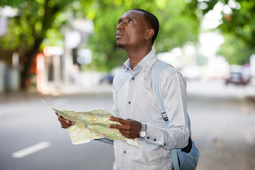 Portrait of a young tourist man looking for his landmarks with a map in town.