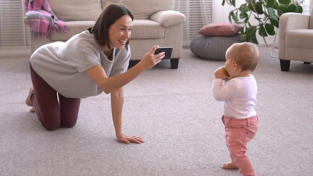 Mother photographing baby girl using mobile phone camera