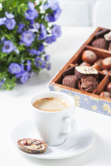 Cup of coffee on a white background with a variety of chocolates in a wooden box.