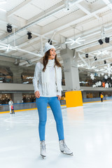 cheerful young woman in white sweater skating on rink alone