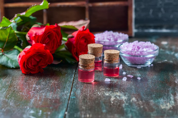 Red roses and bottles of essential oil on dark rustic background, selective focus.